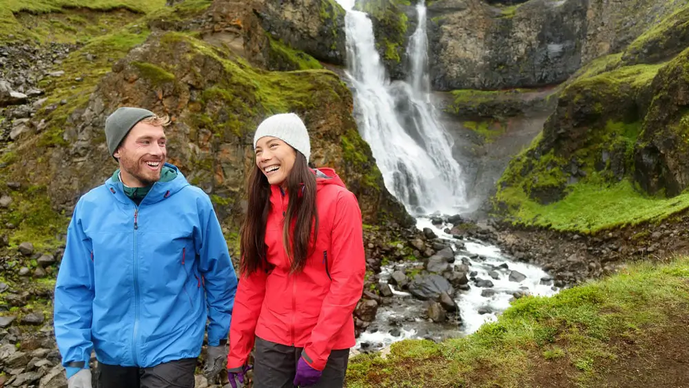 Man and woman in waterproof jackets by a waterfall in Iceland. 