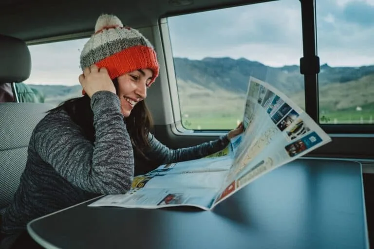 Woman sitting at a table in a campervan, reading a map of Iceland and smiling