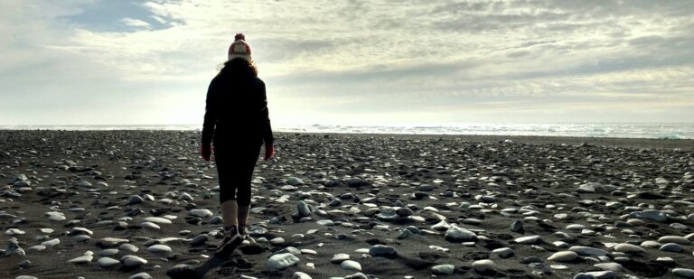 Woman walking on a black beach with rocks