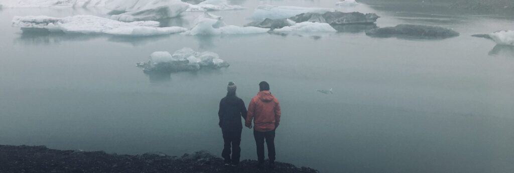 man and woman holding hands looking at lake