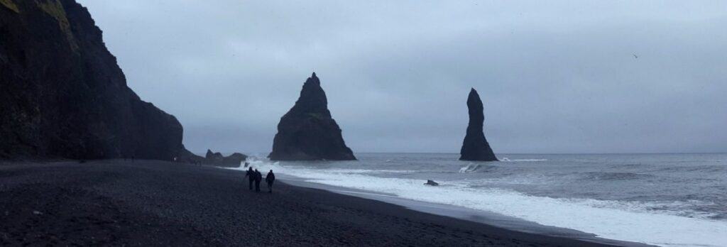 people walking on the black sand beach in Vík í mýrdal