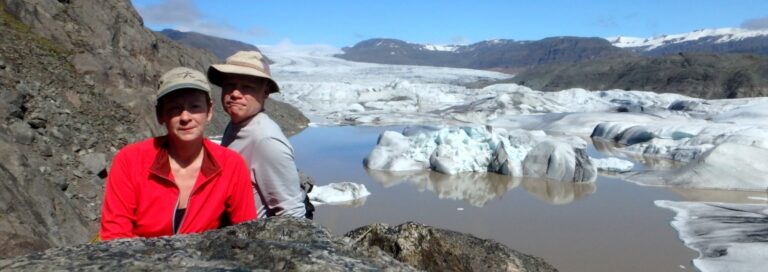 man and woman standing next to cliff and glacier