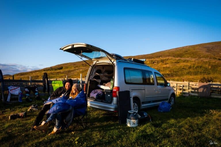 Couple in camping chairs in front of a rent.is camper van
