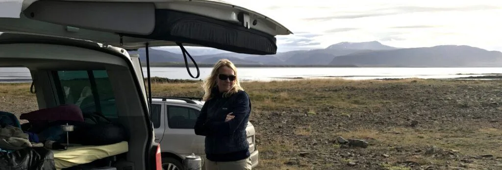 woman with sunglasses standing next to open rent.is camper