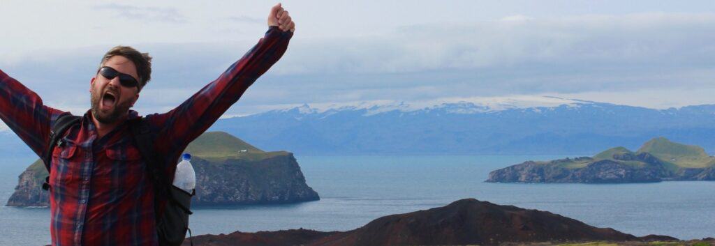 man holding out arms in front of heimaey close to westman islands
