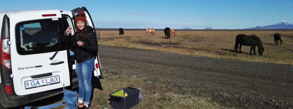 woman standing next to camper car and horses