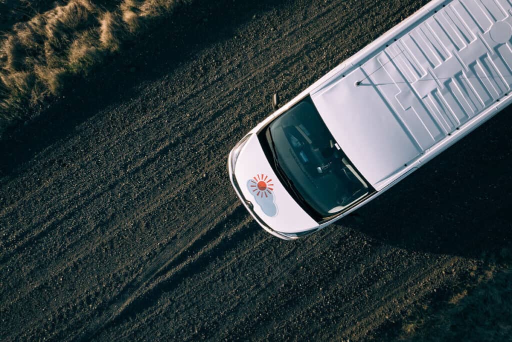 Aerial shot of a Rent.is camper van driving on a gravel road.