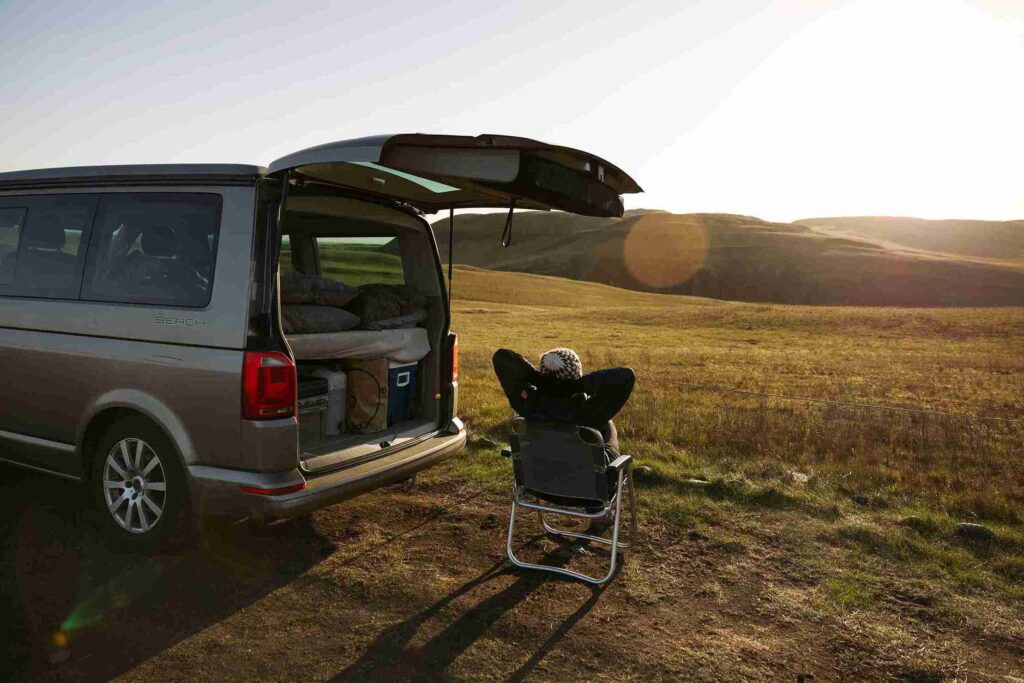 VW California older parked in a field and a woman sitting in the sun