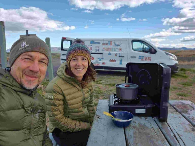 A couple cooking food on a picnic table next to renault trafic