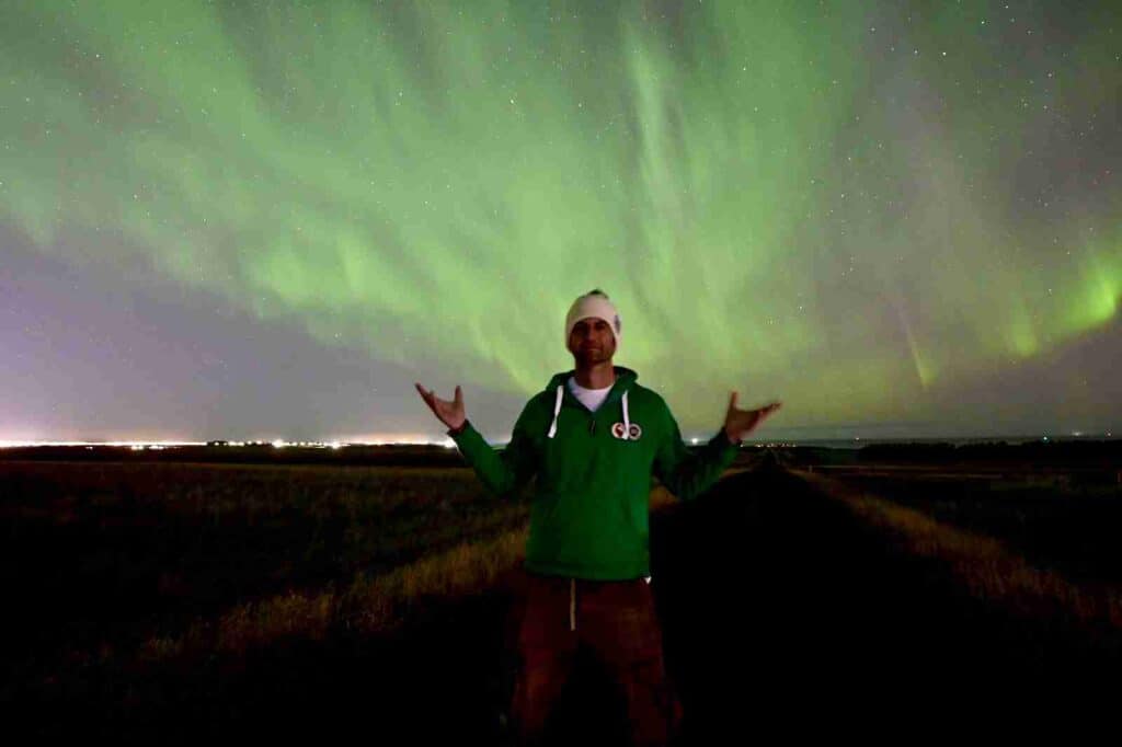 A man standing under green northen lights and stars