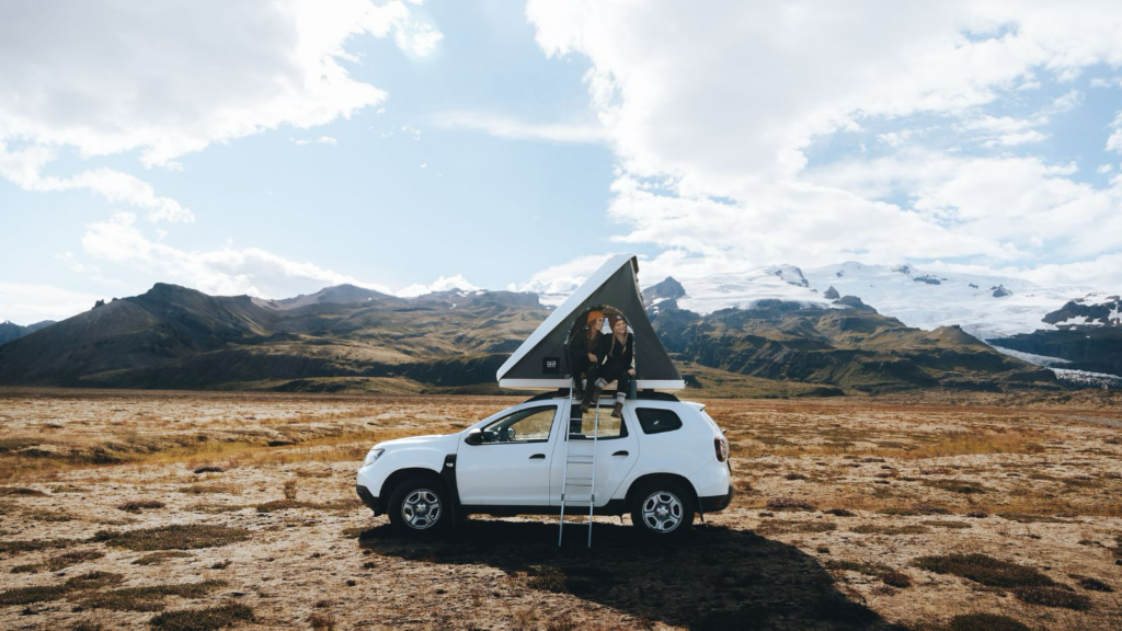 Two people sitting in a rooftop tent of a Dacia Duster in Iceland.