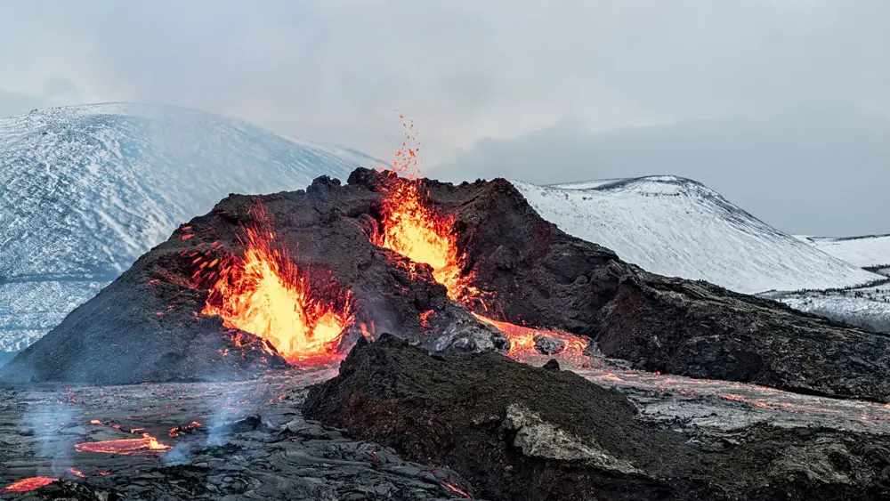 Fagradalsfjall volcanic eruption, Iceland with snowy hills in the background.