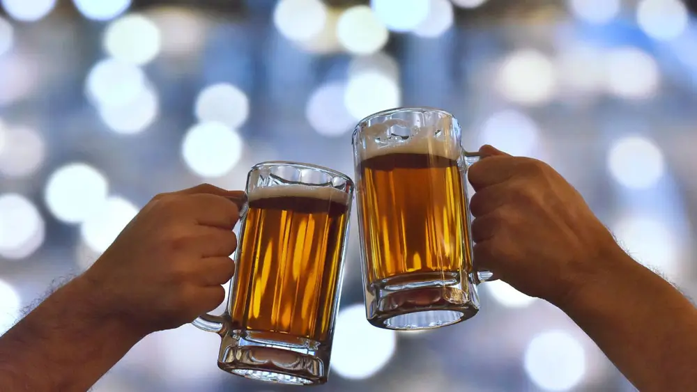 Two people sharing a toast with beer in glass steins.