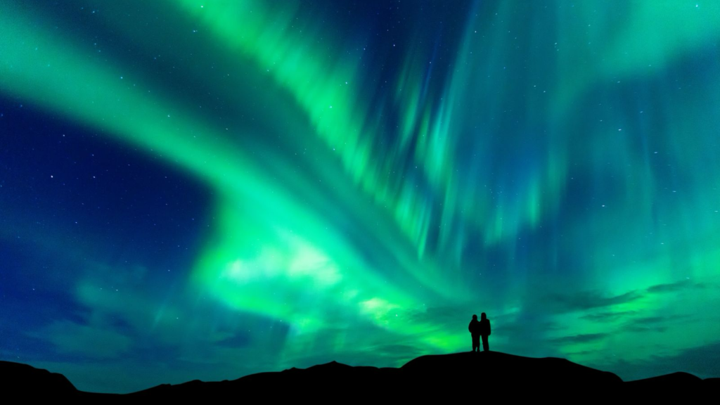 Northern lights in Iceland over a couple standing on a hill.