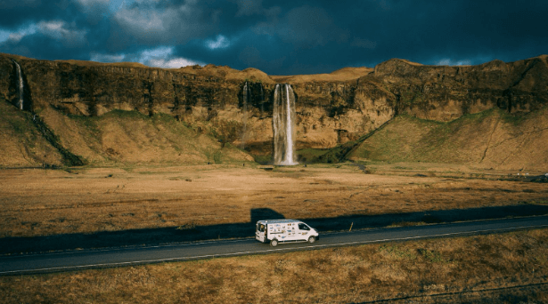 Camper van driving on the road past Seljalandsfoss waterfall in Iceland