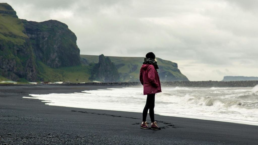 Solo traveler in Iceland standing on black sand beach. 