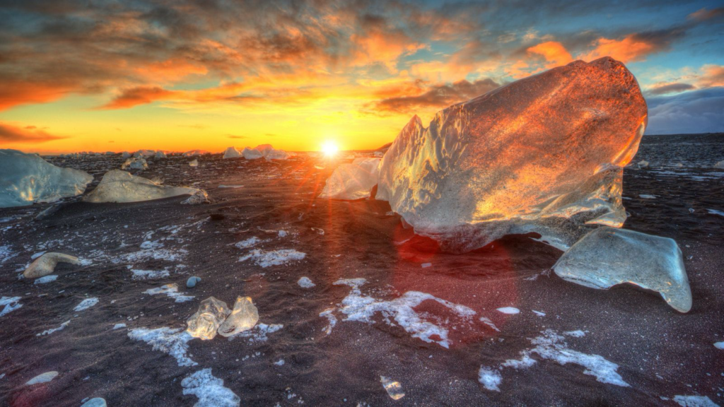 Sun setting on Diamond Beach, Iceland, illuminating chunks of ice on the sand.
