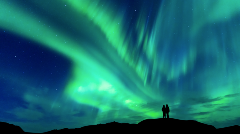 Couple standing on a hill beneath the Northern Lights in Iceland.
