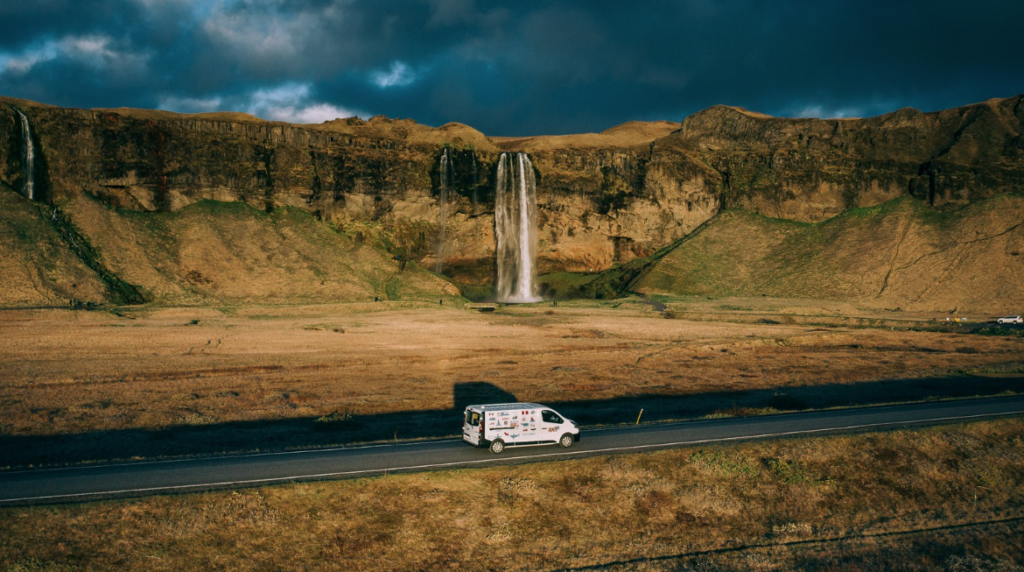 Campervan on Icelandic road driving past Seljalandsfoss waterfall.