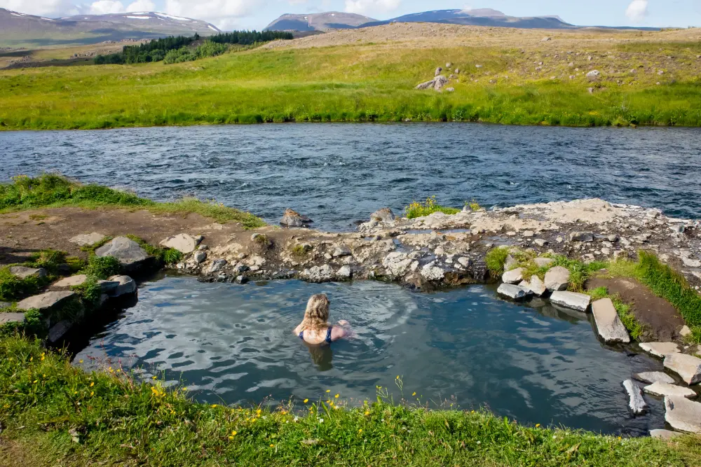 Woman relaxing in an outdoor hot spring in Iceland with a volcanic landscape in the background