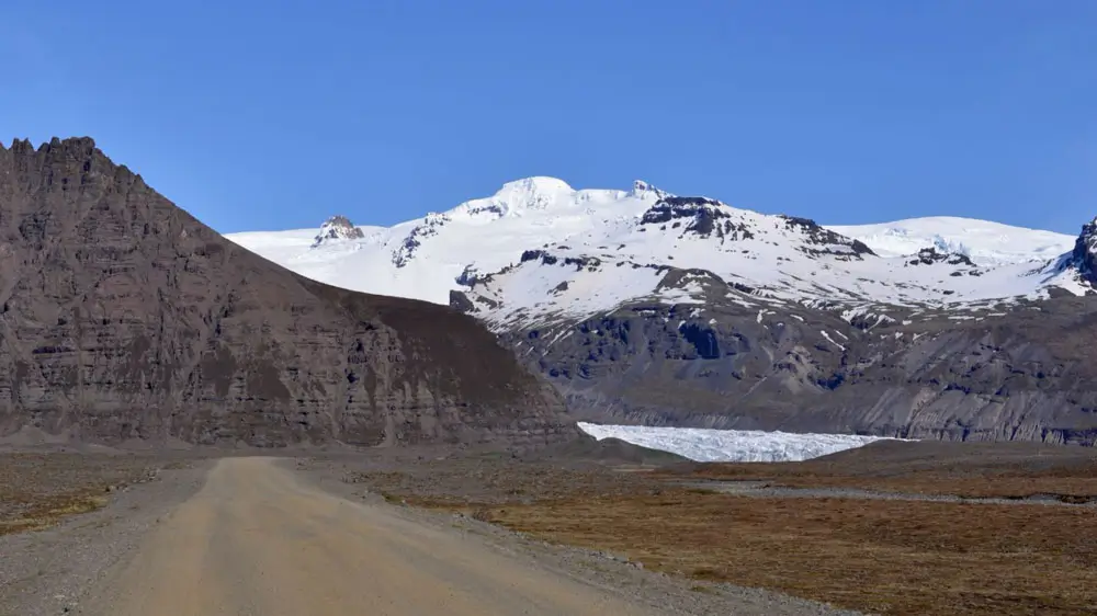 Gravel road in Iceland with glacier and mountains in the distance.