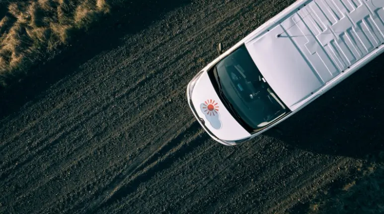 Aerial view of camper van driving on black gravel road.