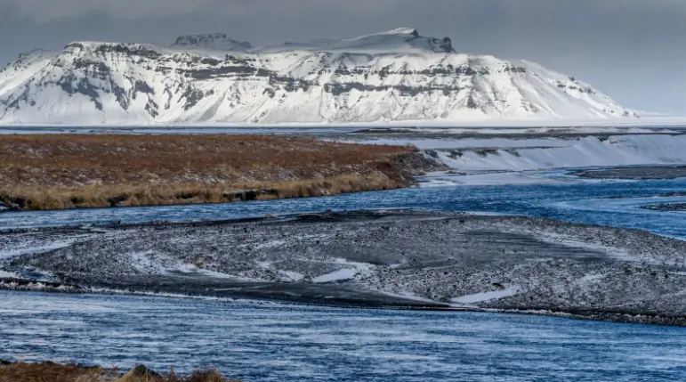 Icelandic landscape with river in the foreground and snow-capped mountains in the background