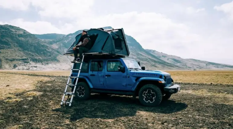 Jeep Wrangler 4xe set up with rooftop tent and ladder in a rugged landscape.