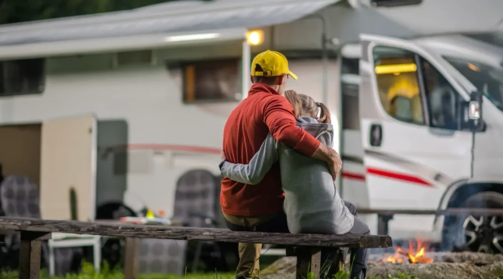 Father and daughter by the campfire outside a motorhome.