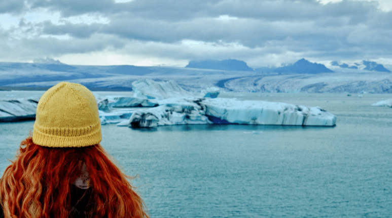 Woman with red hair and a yellow hat standing in front of Jökulsárlón Glacier Lagoon in Iceland.