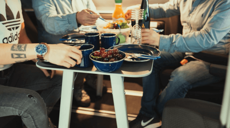 Group of people eating around a camper van table. 