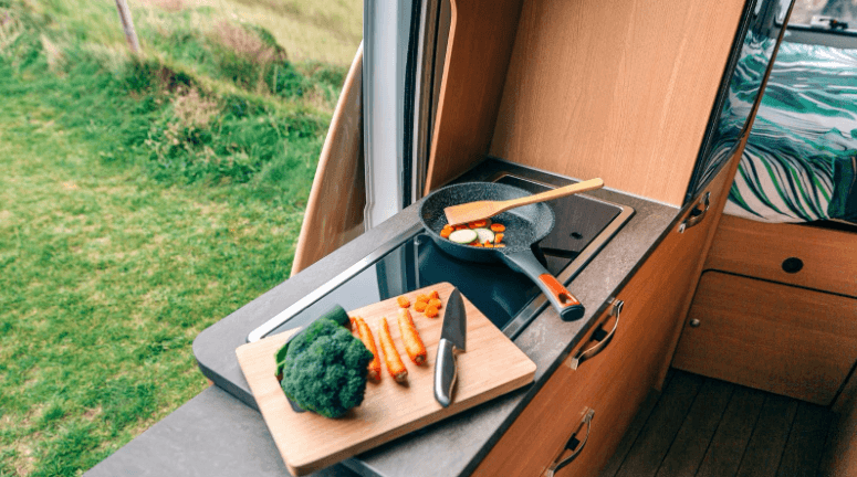 Vegetables on a chopping board and cooking in a pan in a camper. 