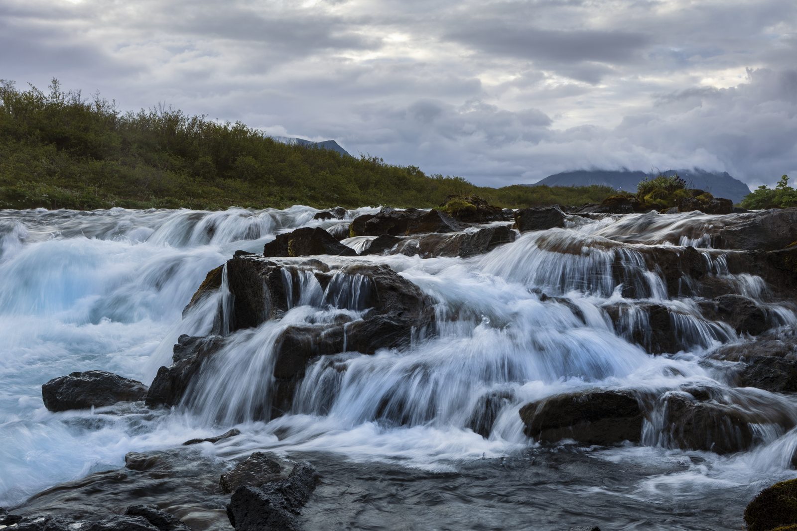 Wide cascades of white water over dark rocks on the Brúará river in Iceland