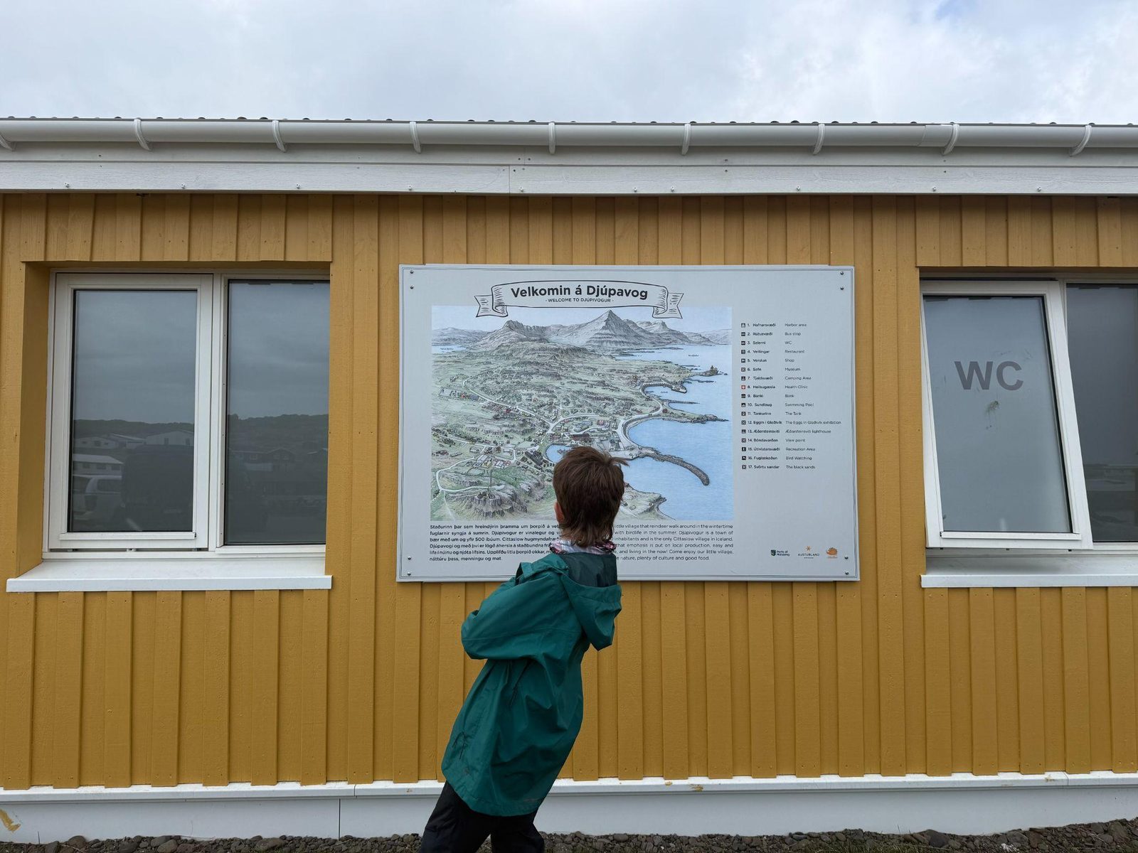 Child reading the welcome map sign in the fishing town of Djúpivogur