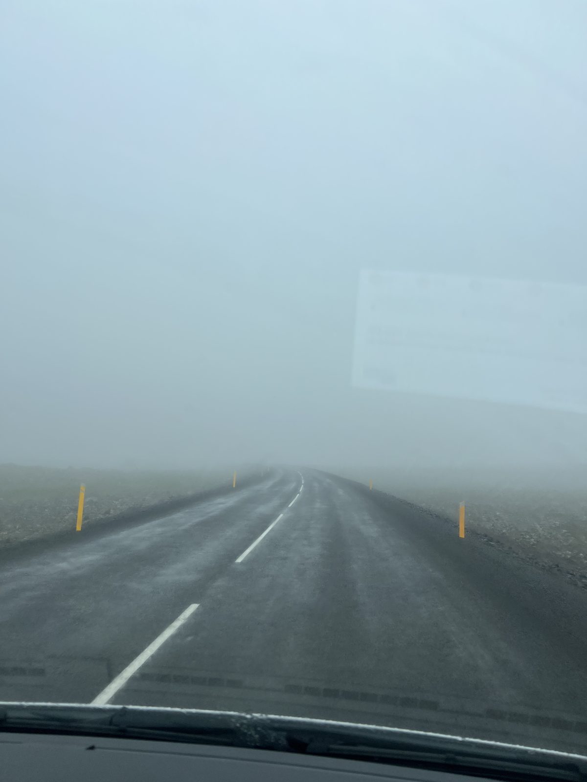 View through the windscreen of a road disappearing into thick fog in the Westfjords