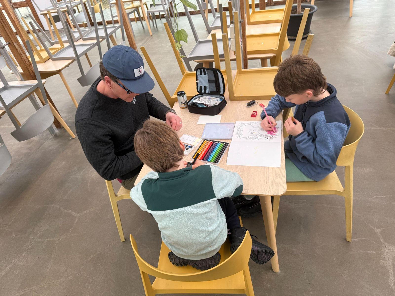 Dad and two kids colouring at a café table during their Iceland campervan trip