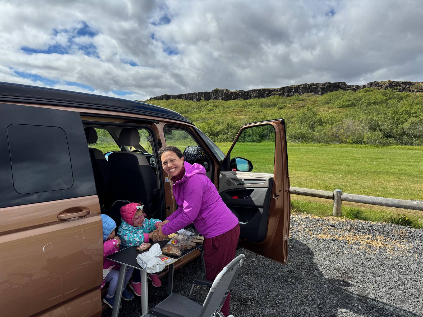 Mother and toddlers having a picnic beside the open door of a VW California Beach camper van near Þingvellir