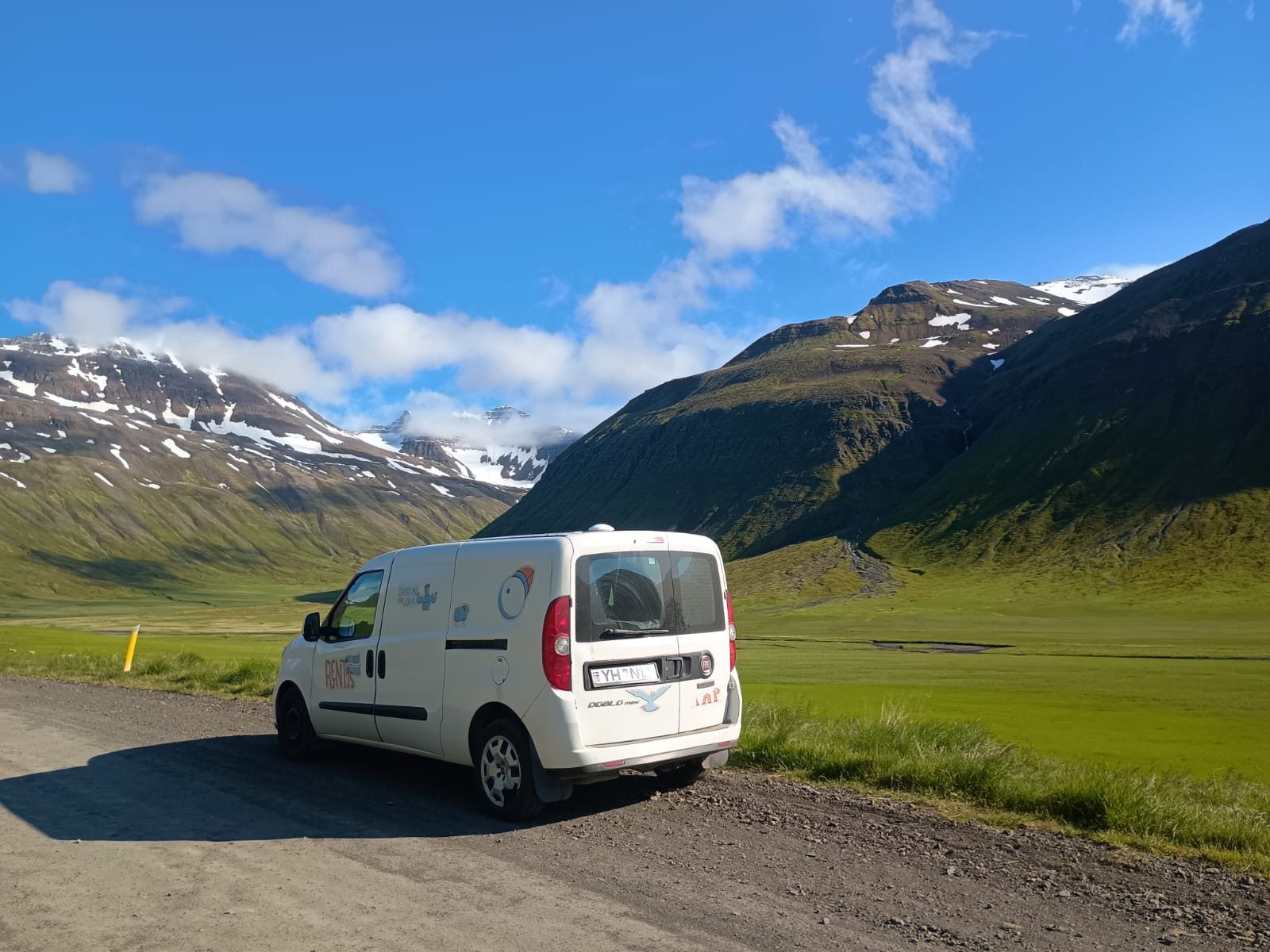 Camper on a gravel road in a green valley beneath snow-streaked mountains in Iceland