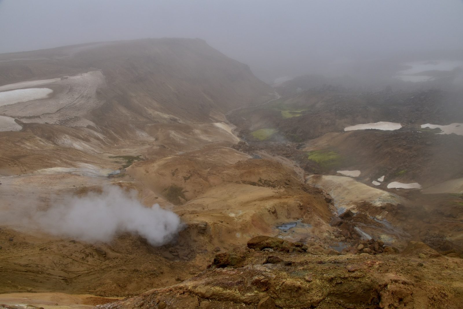 Steam rising from ochre geothermal hills with snow patches in the Icelandic Highlands
