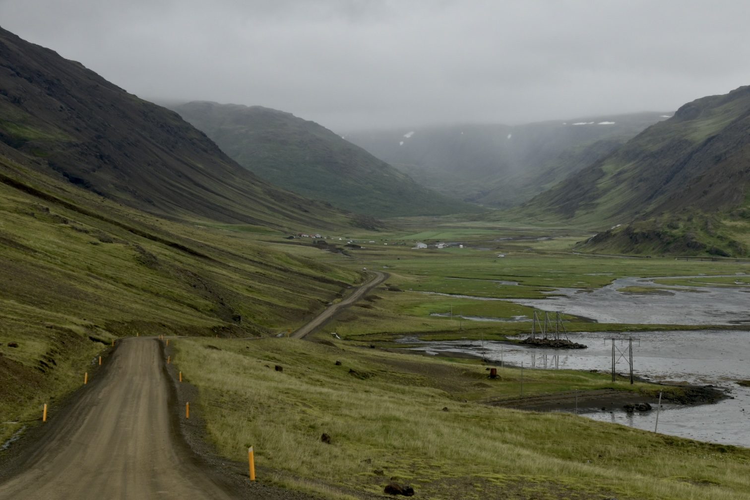 Gravel road winding down into a green valley with a river in the Westfjords