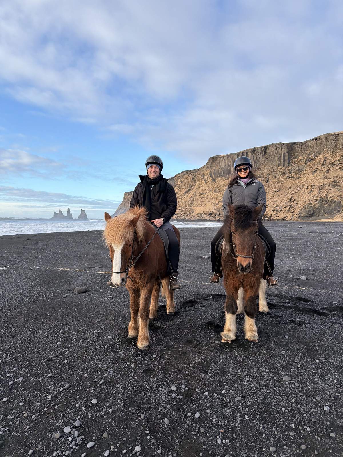 Riding Icelandic horses on a black sand beach with the Reynisdrangar sea stacks behind