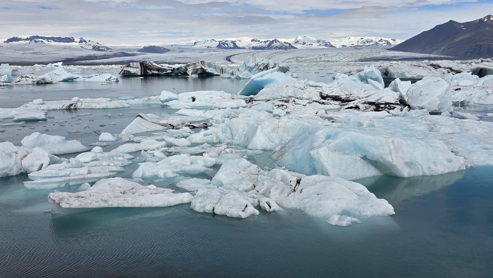 Blue and white icebergs drifting across Jökulsárlón Glacier Lagoon with mountains behind