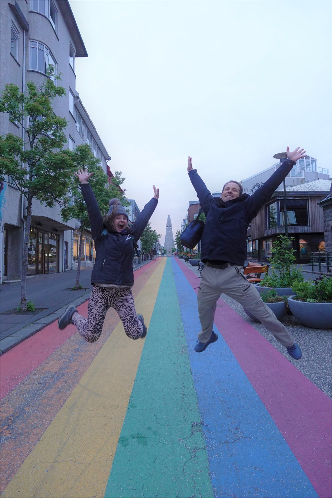 Two travellers jumping for joy on the rainbow-painted street in Reykjavík