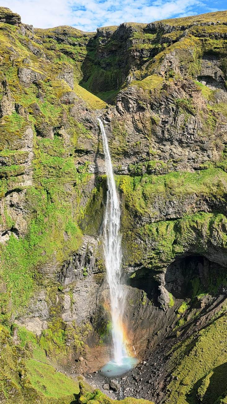 Tall waterfall with a rainbow plunging into the mossy Múlagljúfur canyon in Southeast Iceland