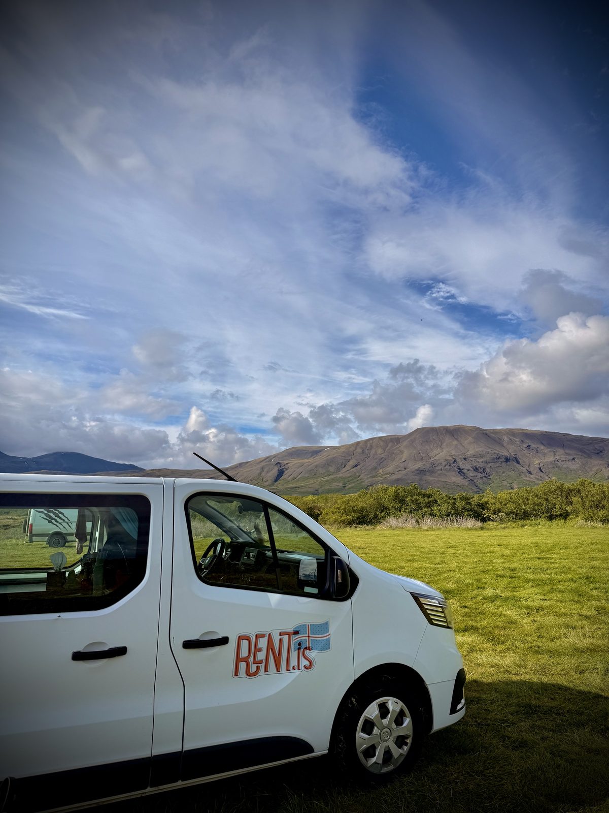 Renaldo, the Rent.is Renault camper van, parked on green grass under a blue sky in Iceland in June