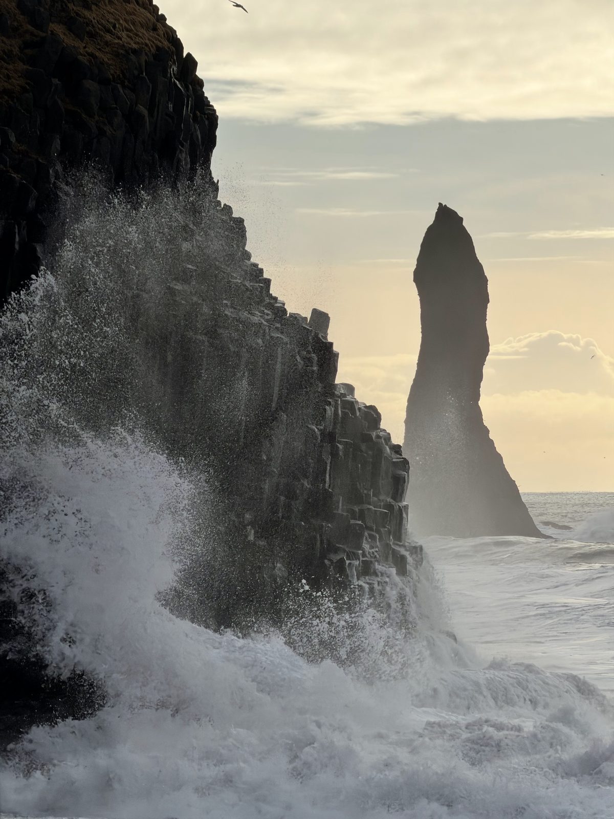 Waves crashing against the basalt columns at Reynisfjara with a sea stack behind