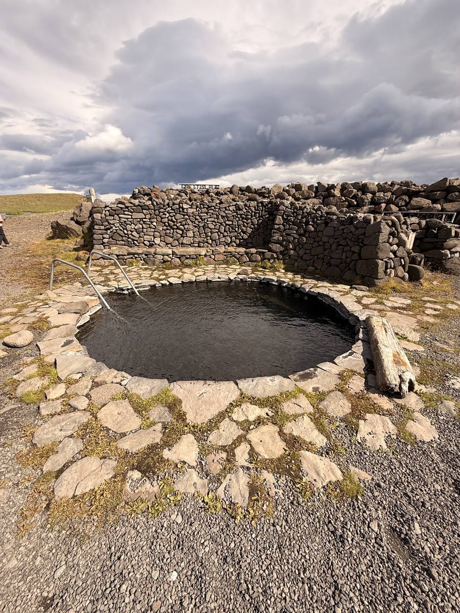 Round natural hot pool surrounded by a stone wall in North Iceland
