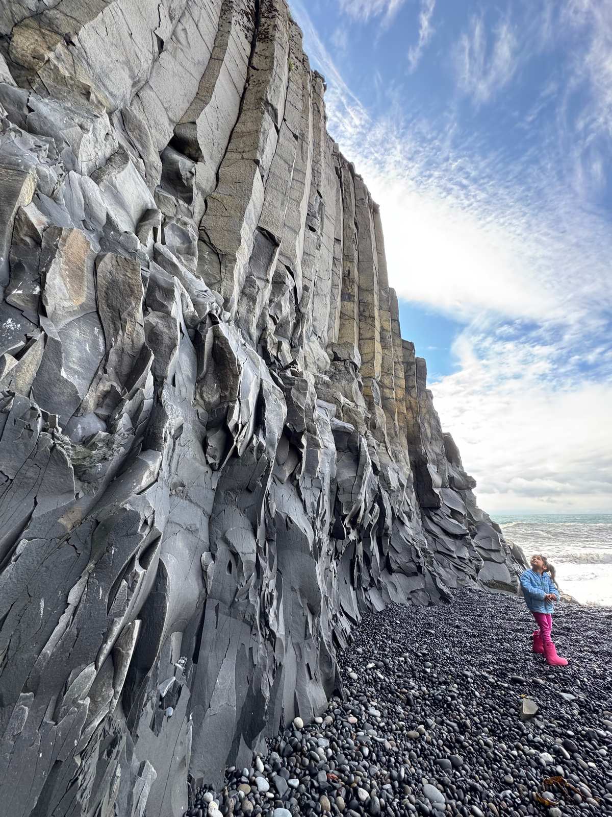 Small child beneath towering basalt columns at Reynisfjara black sand beach