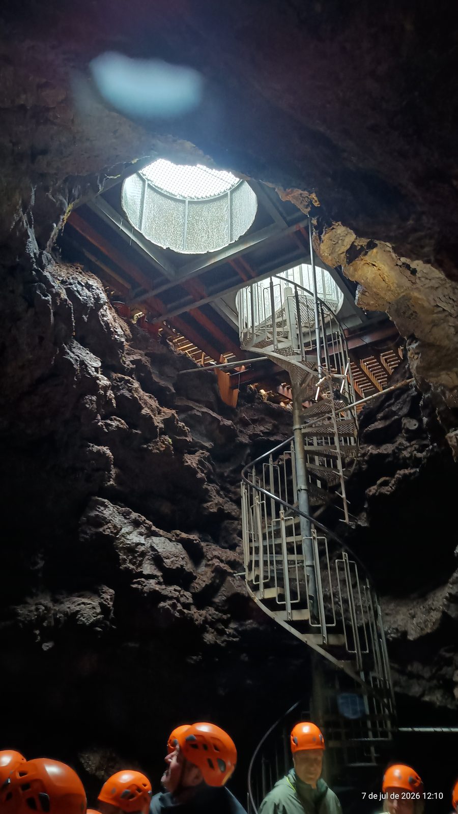 Spiral staircase leading down into Vatnshellir lava cave, with visitors in helmets