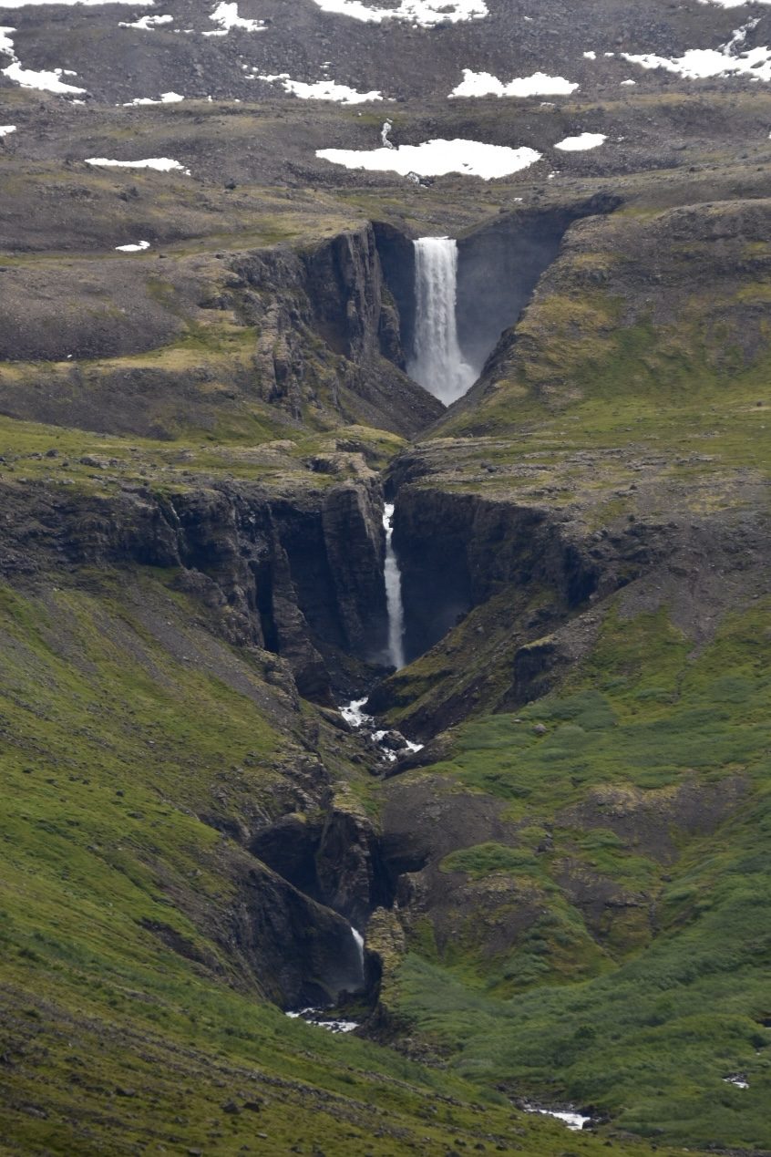 Chain of waterfalls tumbling down a green mountain gorge with snow patches in Iceland